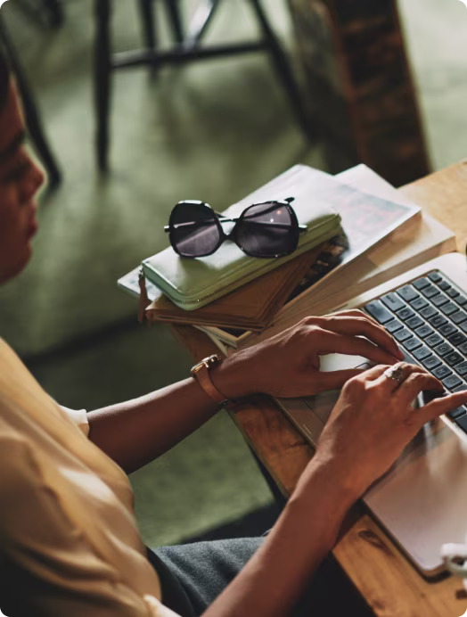 Mãos digitando no notebook, com óculos escuros sobre a mesa