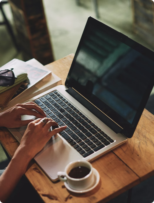 Mãos digitando no notebook ao lado de uma xícara de café